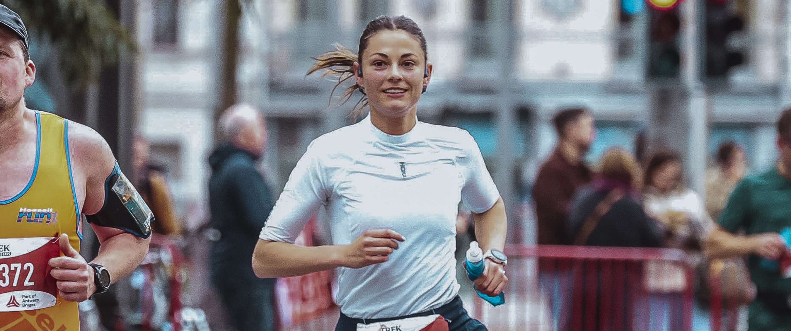 Axelle in wit shirt loopt tijdens een hardloopevenement in een stedelijke omgeving.