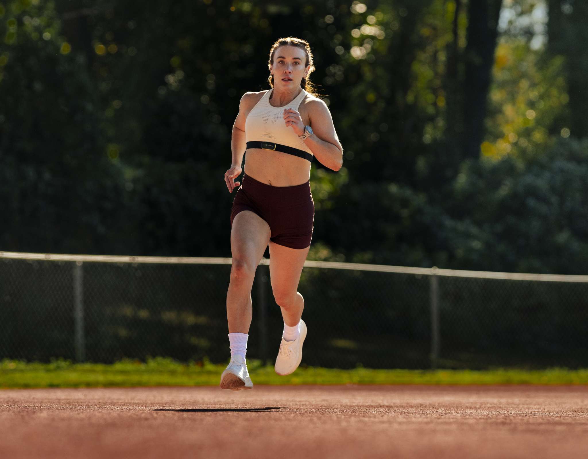 Vrouw rent op een atletiekpiste met sporthorloge en sportkleding in openlucht.