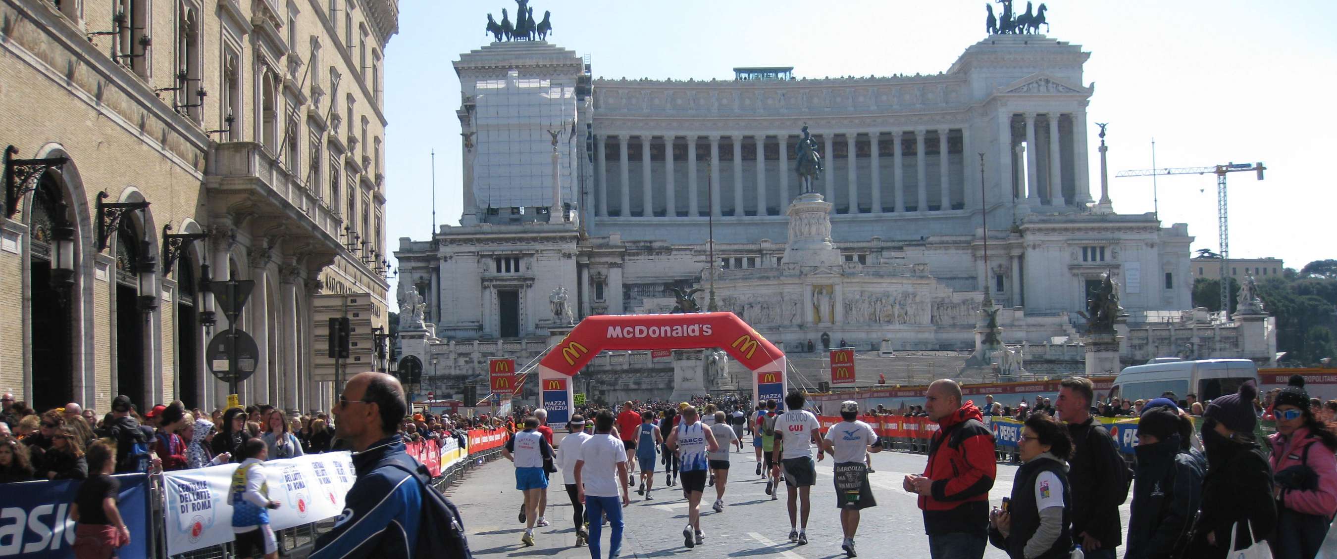 Hardlopers en toeschouwers bij de finish van een marathon op Piazza Venezia in Rome, met zicht op het Vittoriano