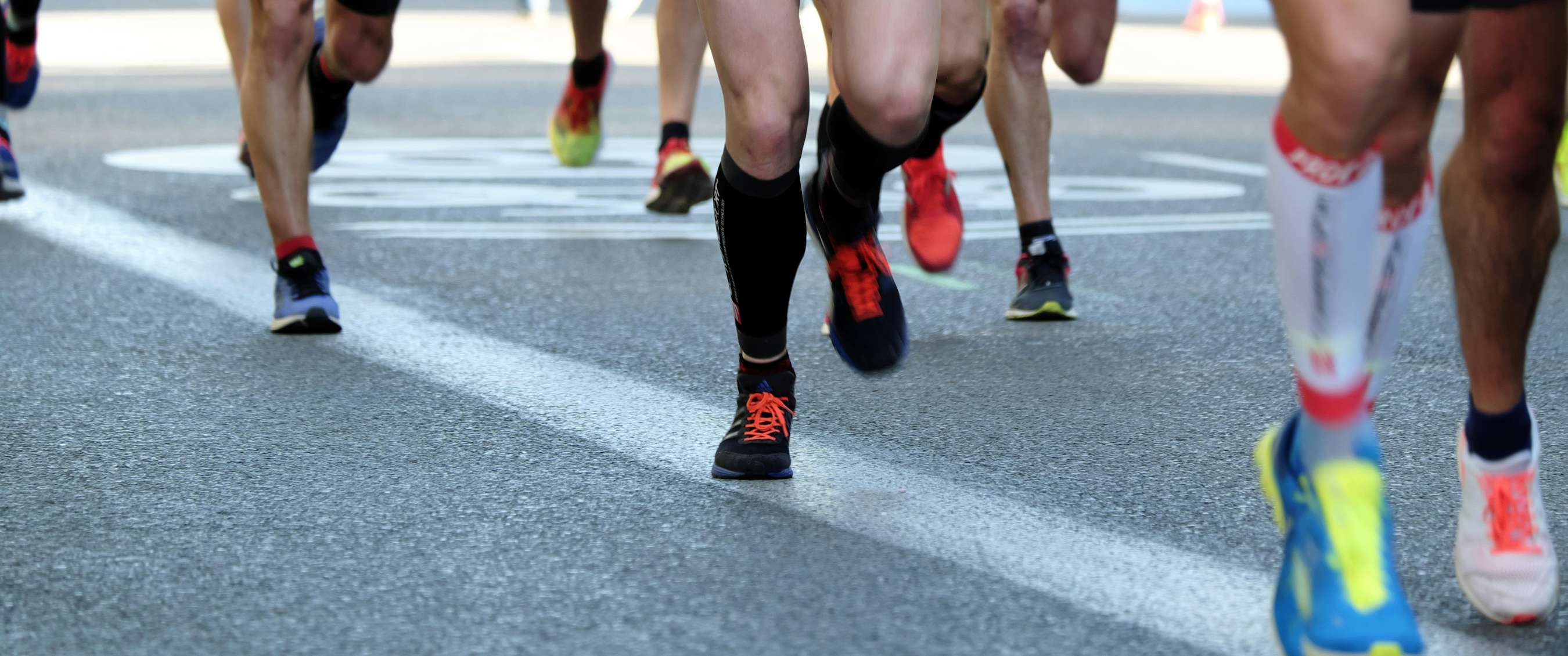 Close-up van hardlopende benen op asfalt tijdens een marathon.
