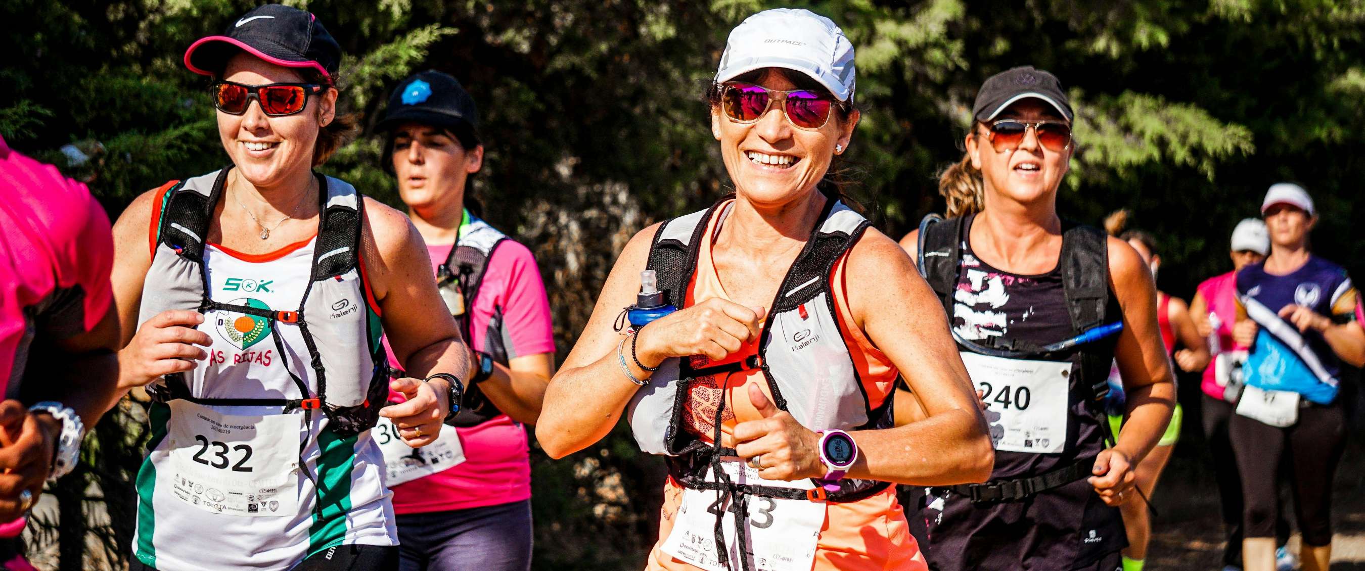 Een groep vrouwelijke deelnemers tijdens een marathon op een zonnige dag, lachend en geconcentreerd.