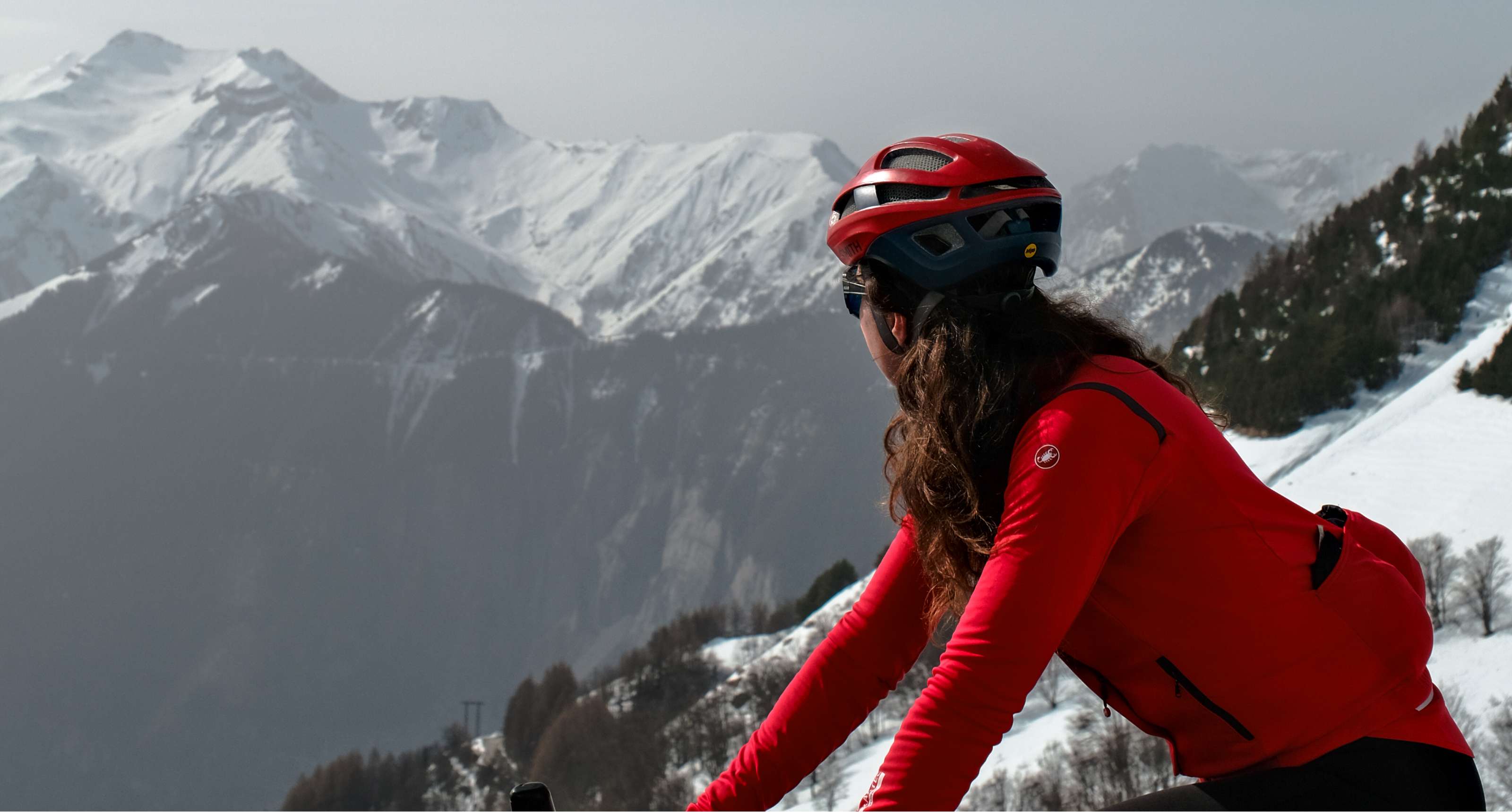 Een fietser met rode helm bewondert een berglandschap met sneeuw op de toppen.