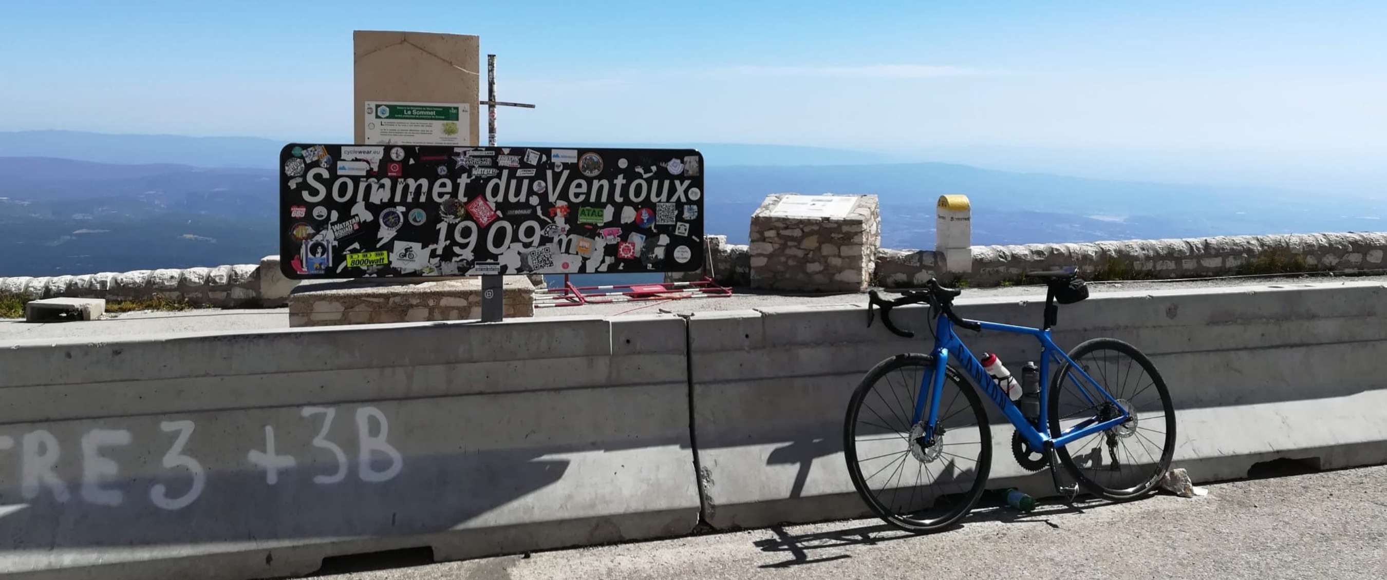 Blauwe racefiets naast het bord “Sommet du Ventoux 1909 m” op een bergtop.
