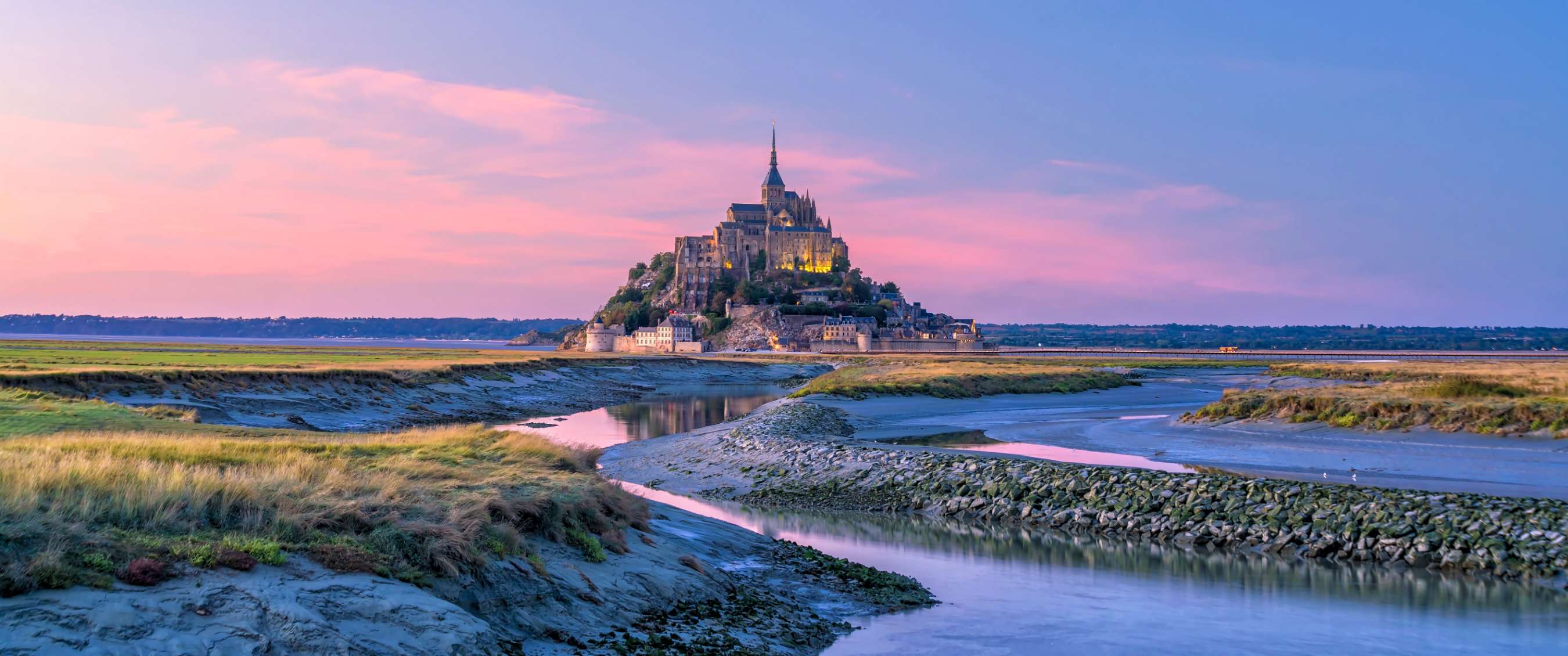 Mont Saint-Michel bij zonsondergang, met water en slikken op de voorgrond