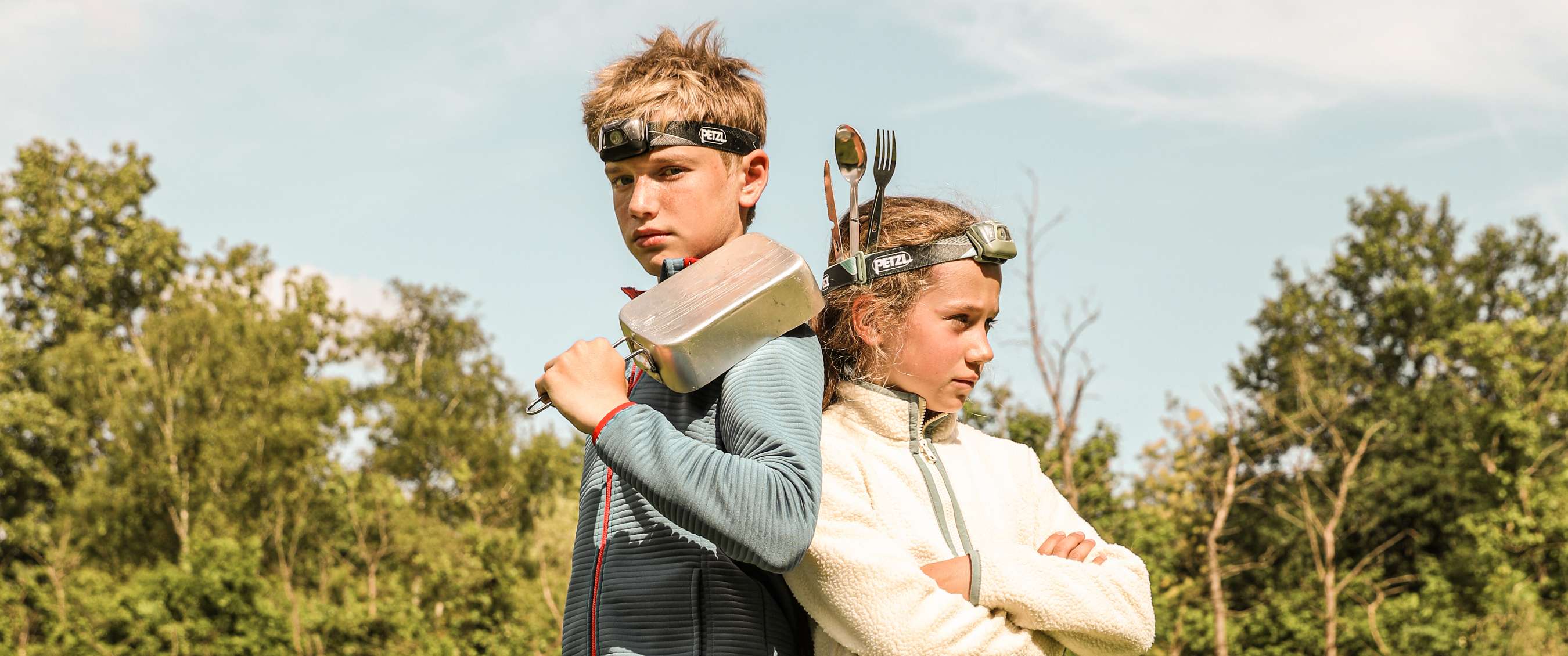 Twee kinderen met Petzl-hoofdlampen poseren rug aan rug in de natuur.