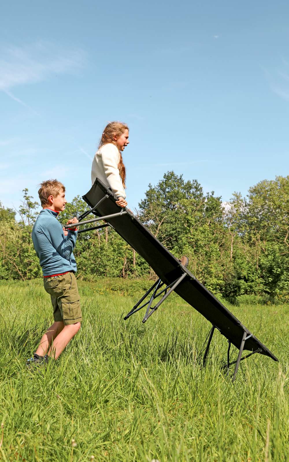 Kinderen spelen met een veldbed in een zonnig grasveld.
