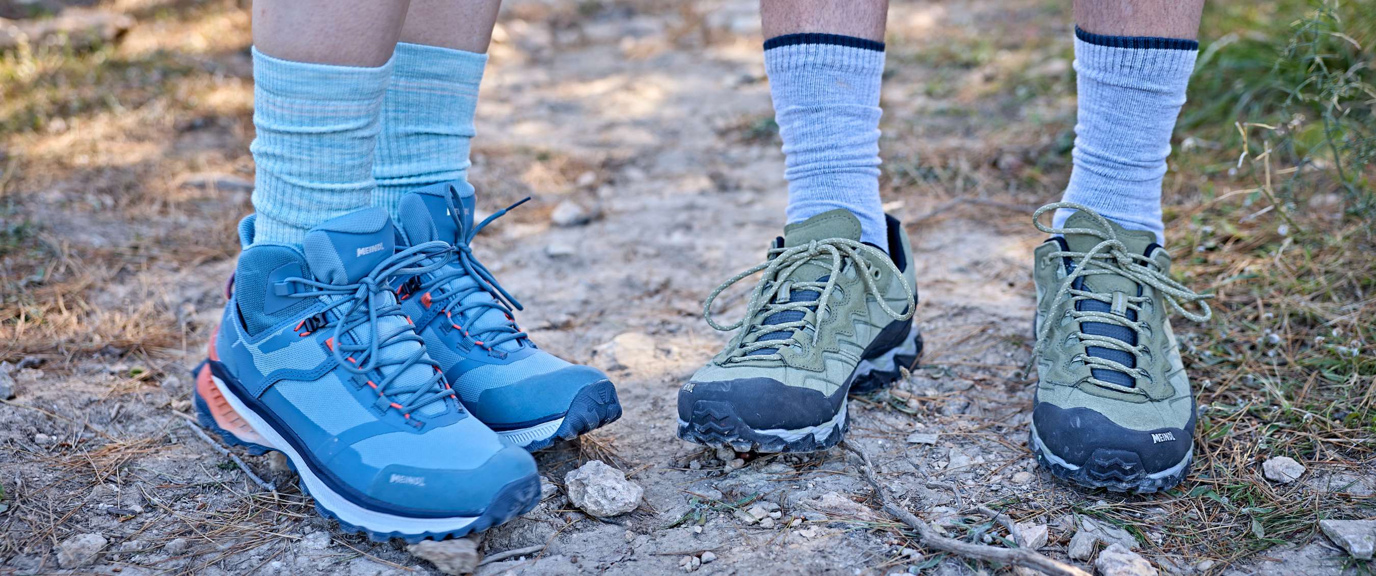 Twee paar wandelschoenen met sokken staan op een droog bospad.