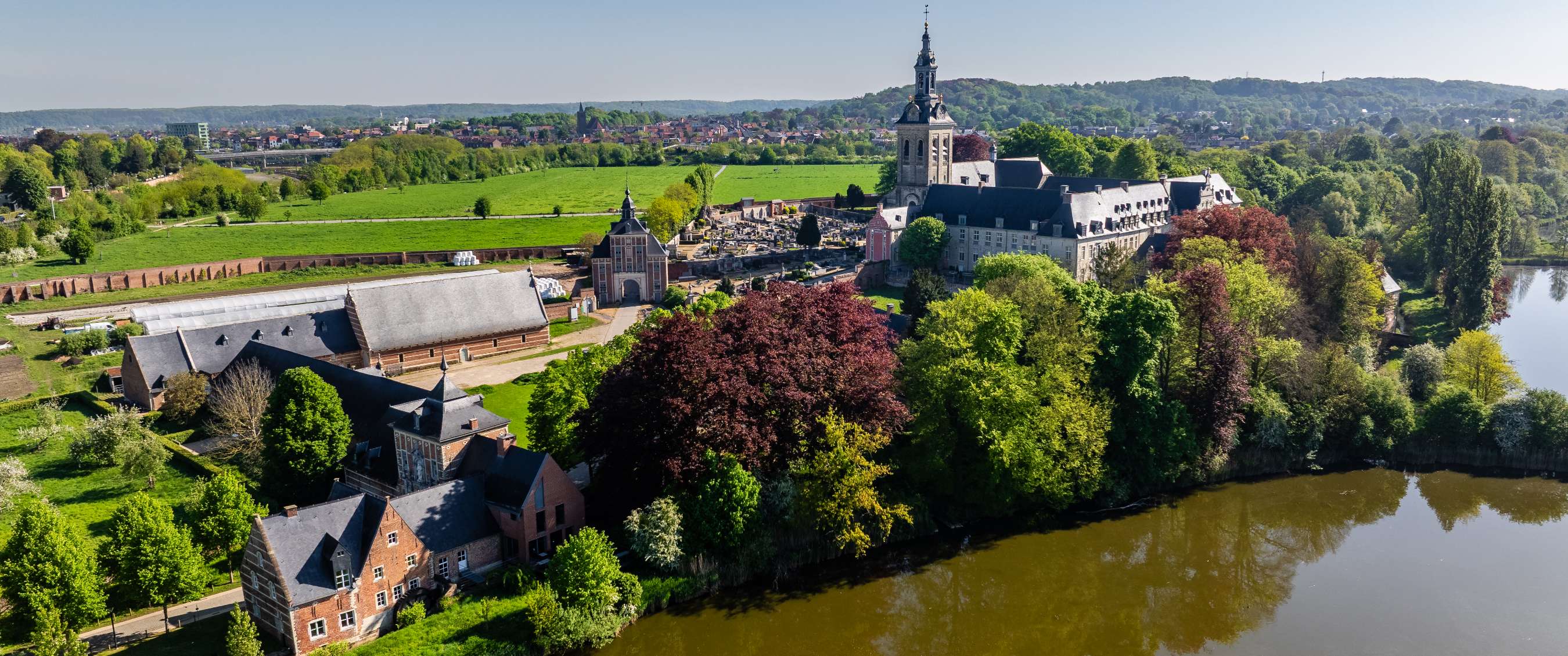 Luchtbeeld van abdijcomplex langs rivier met bomen en velden bij Leuven.