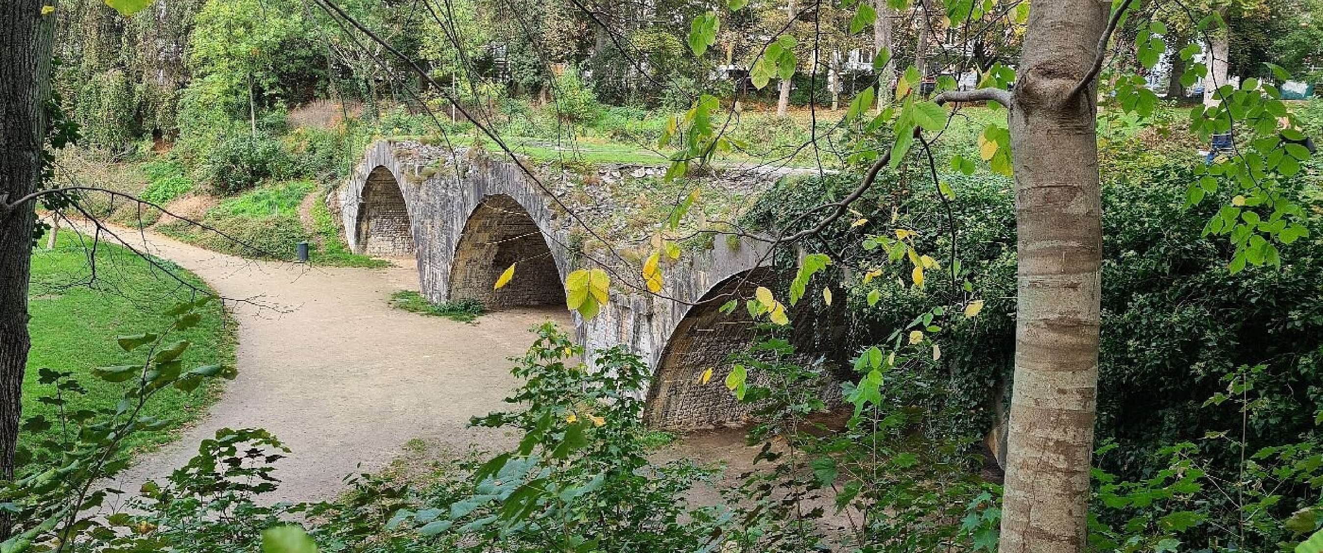 Stenen boogbrug over pad in groen park met bomen in Namen.
