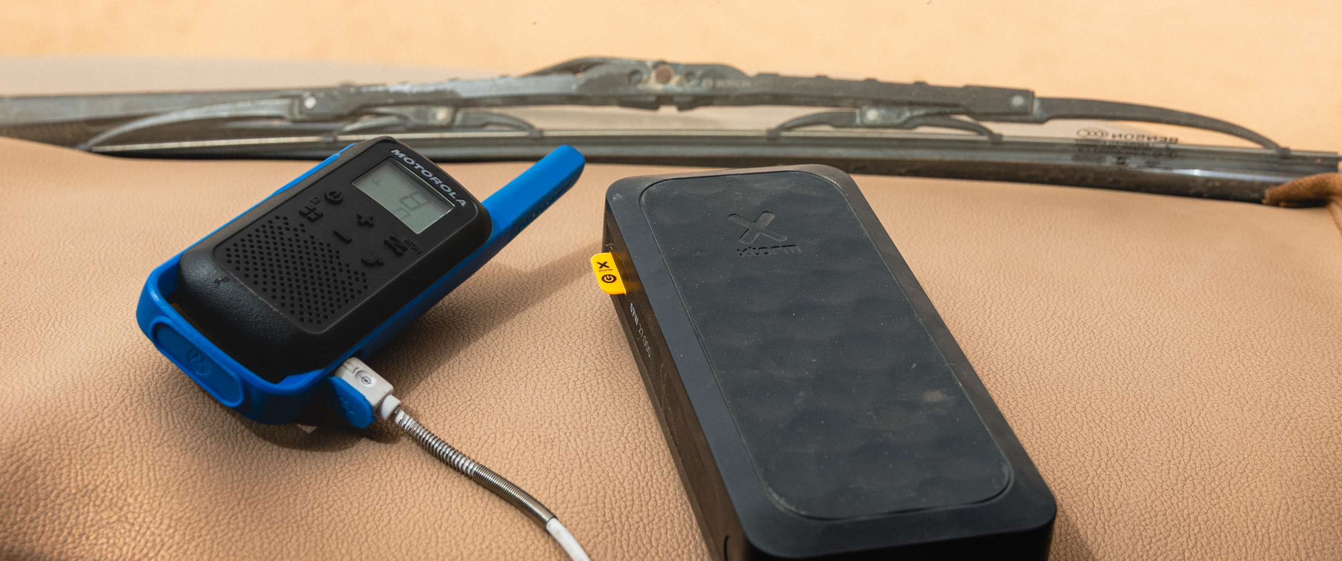Walkietalkie en Xstorm powerbank liggen op het dashboard met ruitenwisser op de achtergrond.