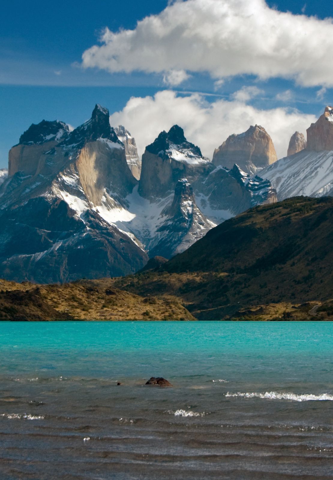 Uitzicht op helderblauw meer met imposante bergen en wolken erboven.