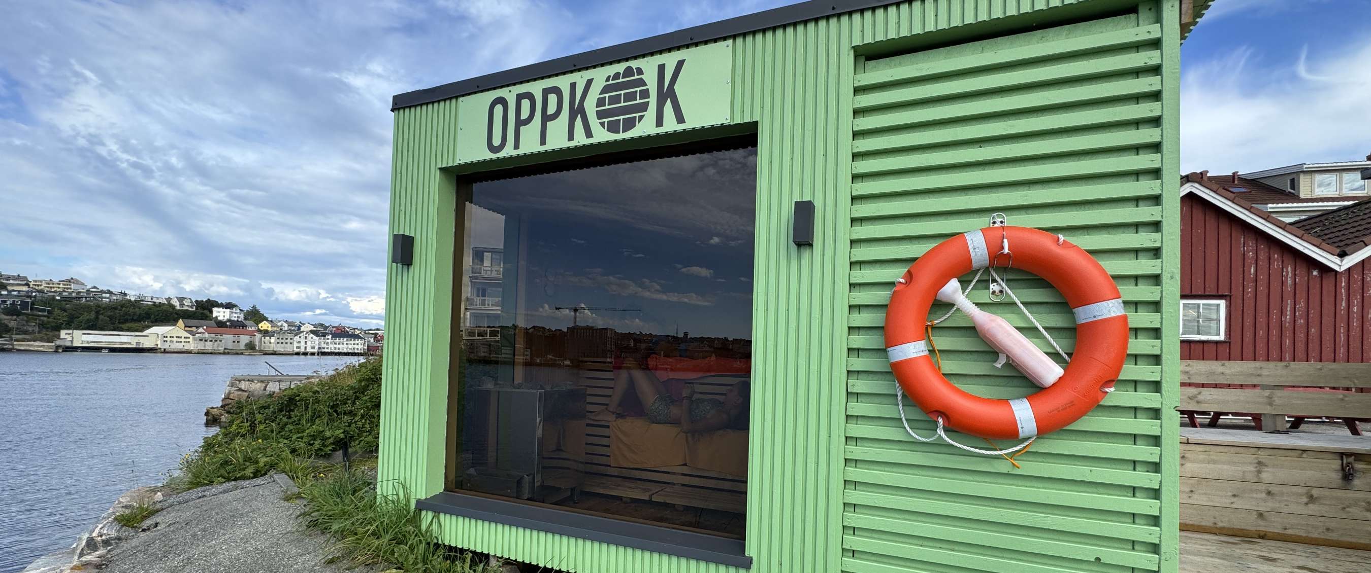 Groen houten gebouw met het opschrift OPPKOK en een oranje reddingsboei aan het water.