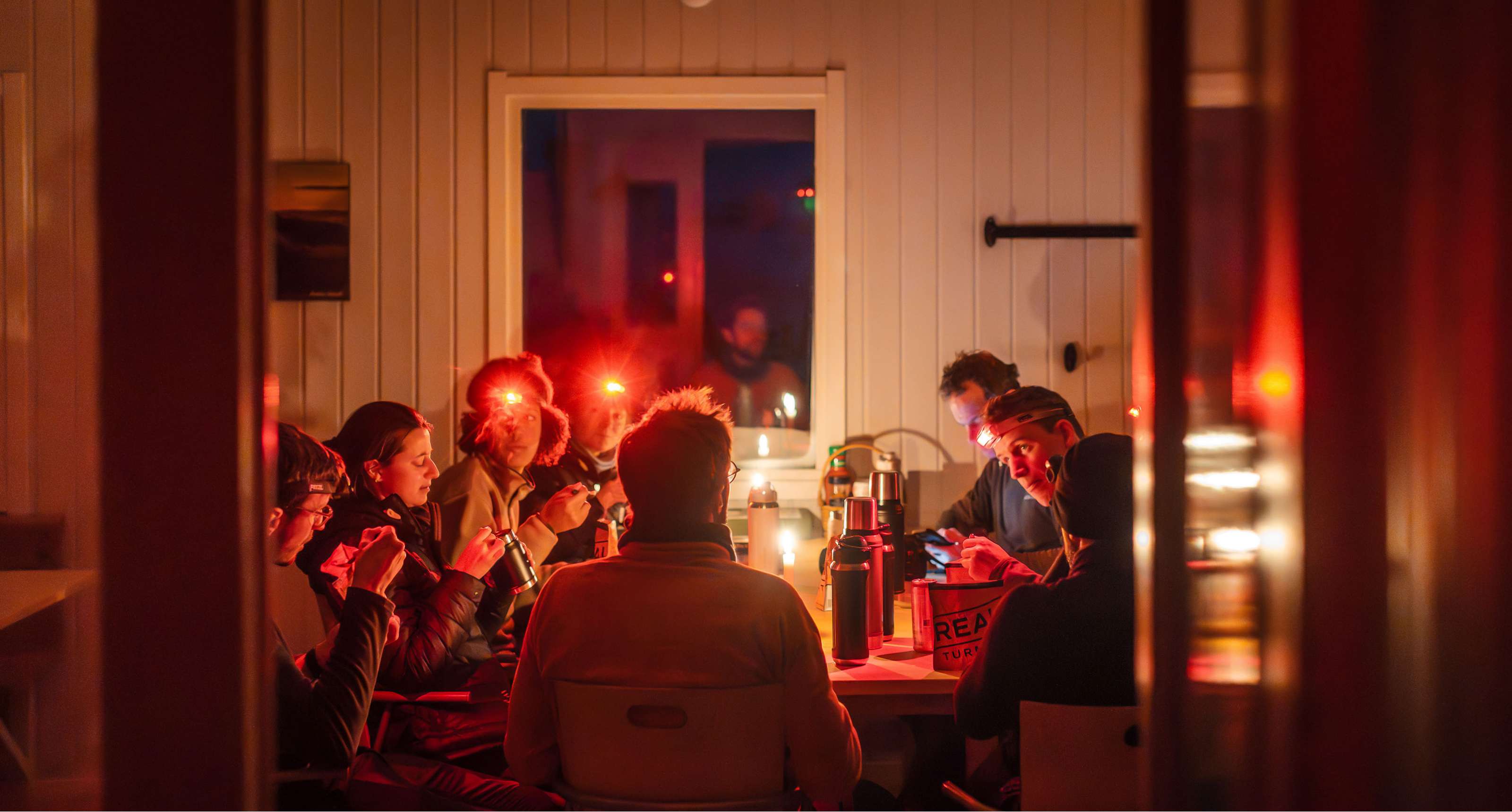 Groep mensen met hoofdlampen eet samen aan een tafel in een warm verlichte houten ruimte.