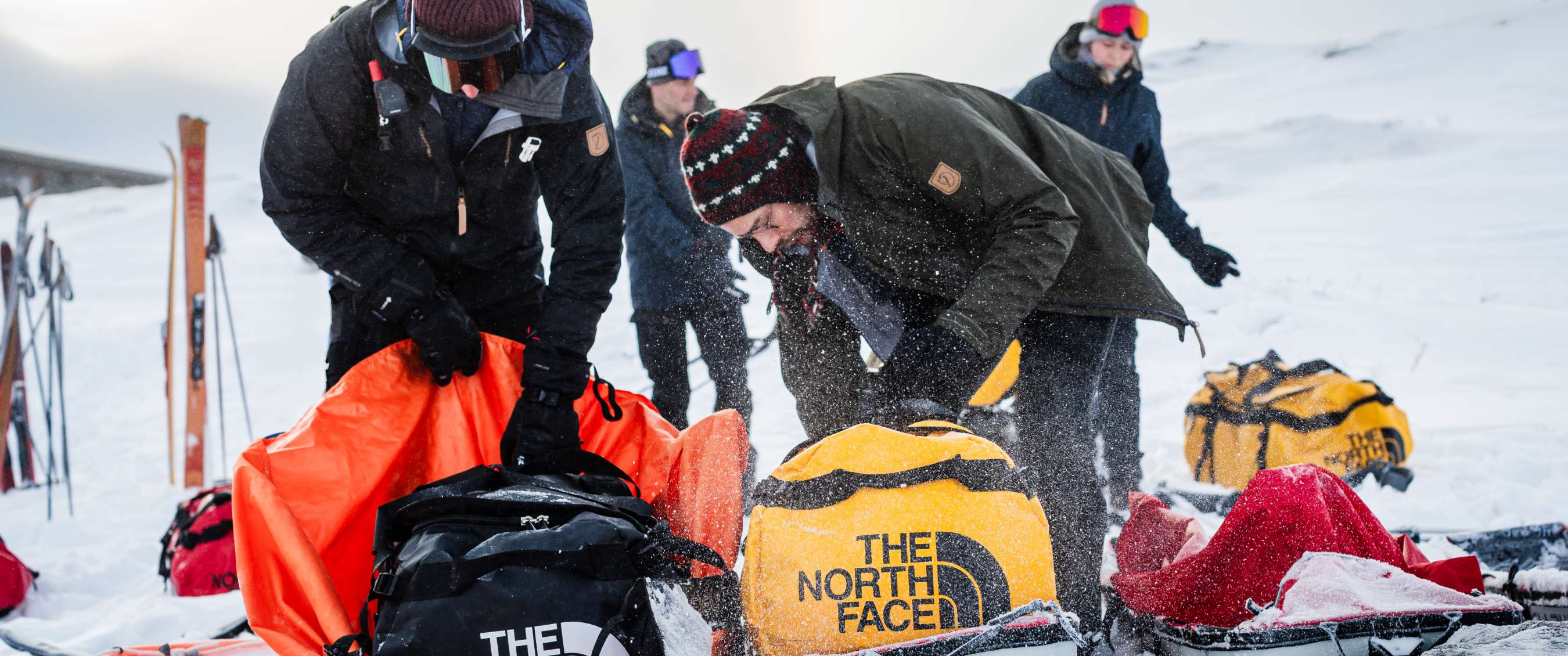 Personen pakken The North Face-duffeltassen uit in een besneeuwd landschap.