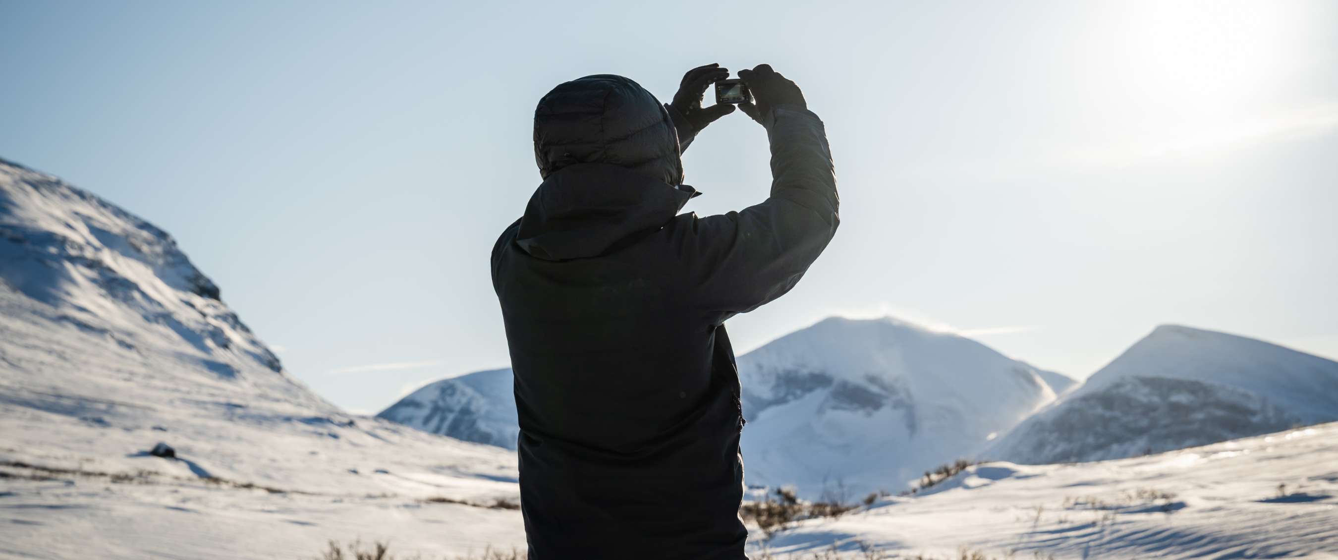 Persoon fotografeert besneeuwde bergen met een kleine camera in de hand