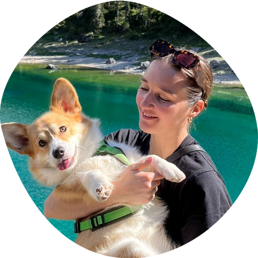  Vrouw houdt een corgi op de arm bij een bergmeer met helderblauw water en dennenbossen. 