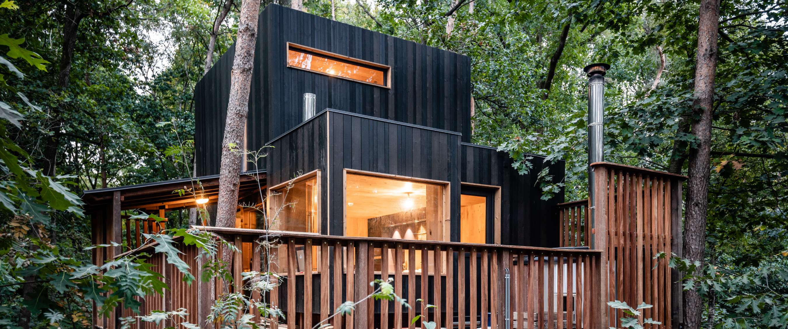 Zwarte houten boshut met grote ramen en houten balustrade