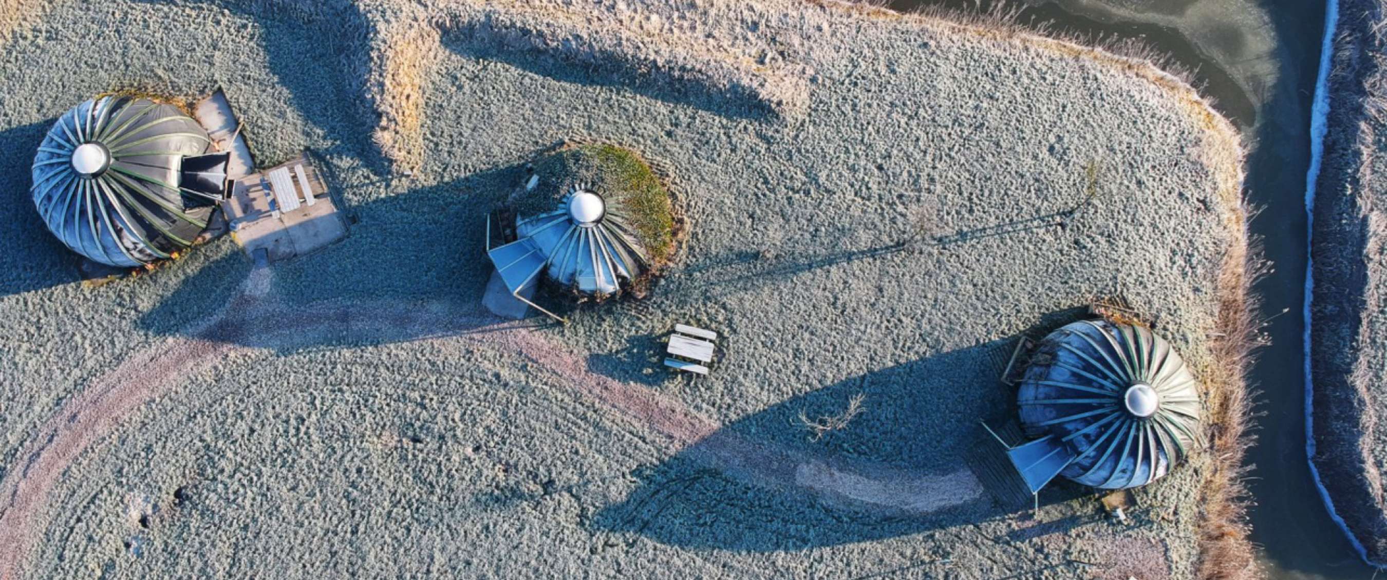 Luchtfoto van ronde vakantiehuisjes met metalen dak, verspreid in een open landschap met rijp op de grond.