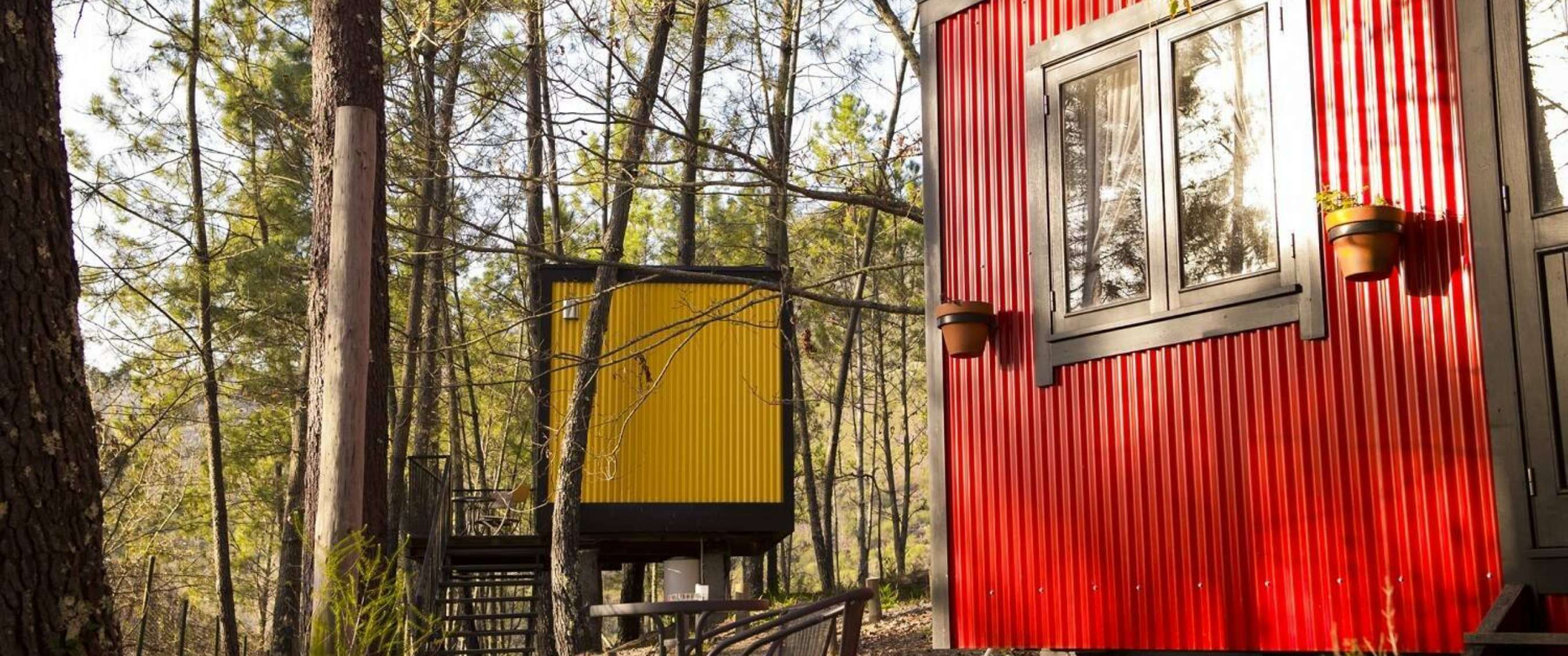Compacte cabins op palen in een bosrijke omgeving, met opvallende rode en gele buitenwanden.