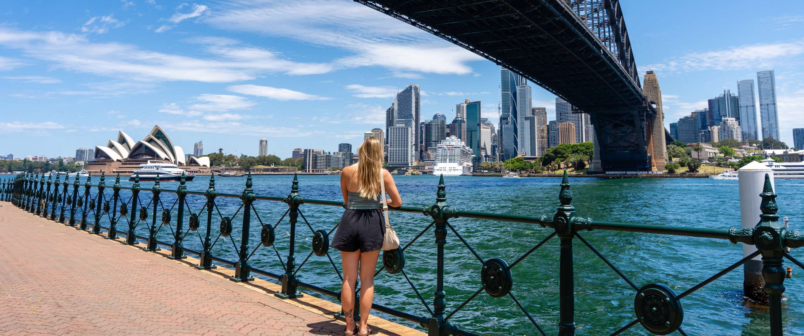 Persoon kijkt uit over de haven van Sydney met Opera House en Harbour Bridge