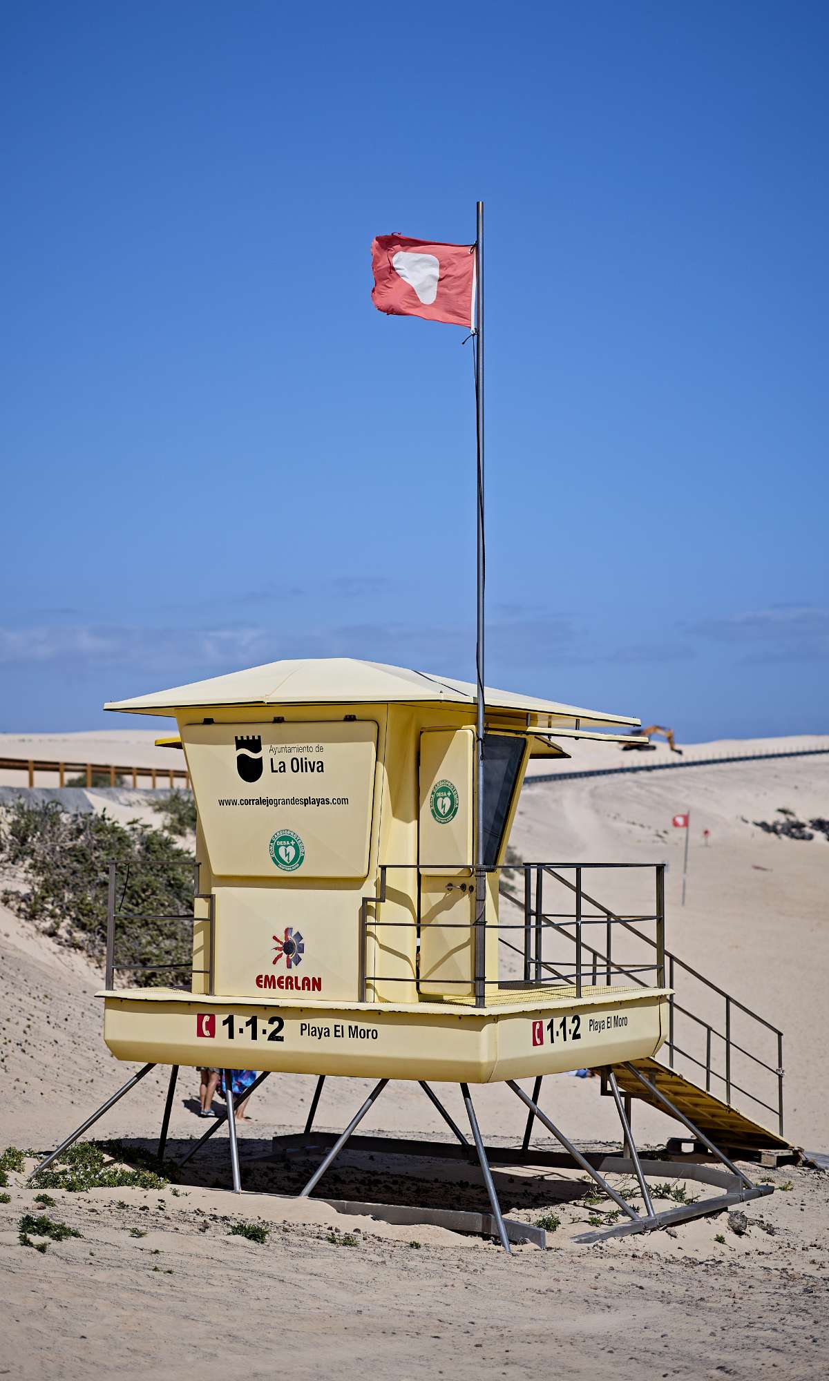 eddingspost op zandstrand met rode vlag erboven en tekst 1-1-2 Playa El Moro.