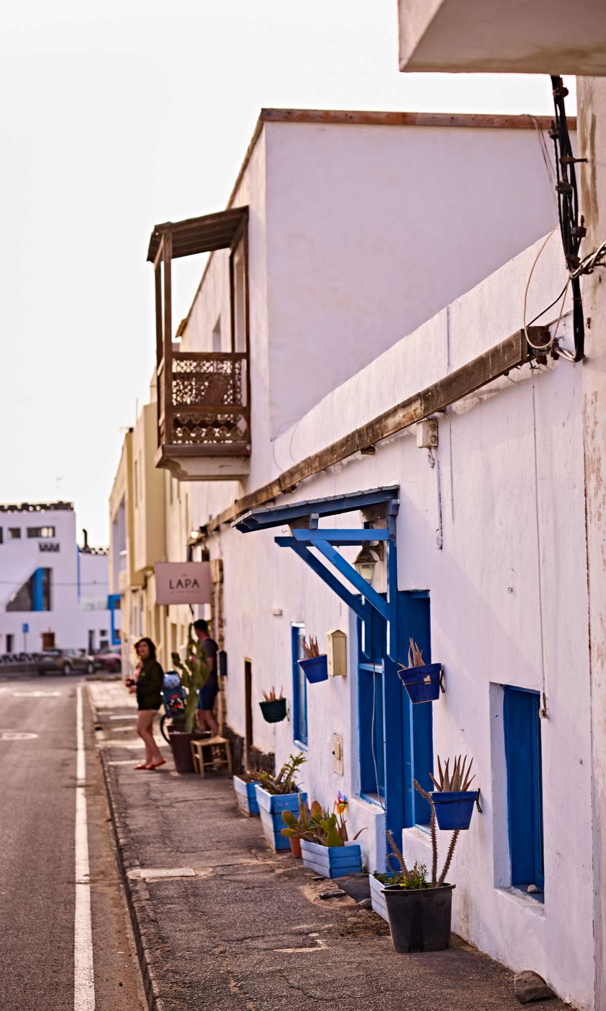 Witte gevel met blauwe ramen en bloempotten langs een rustige straat.