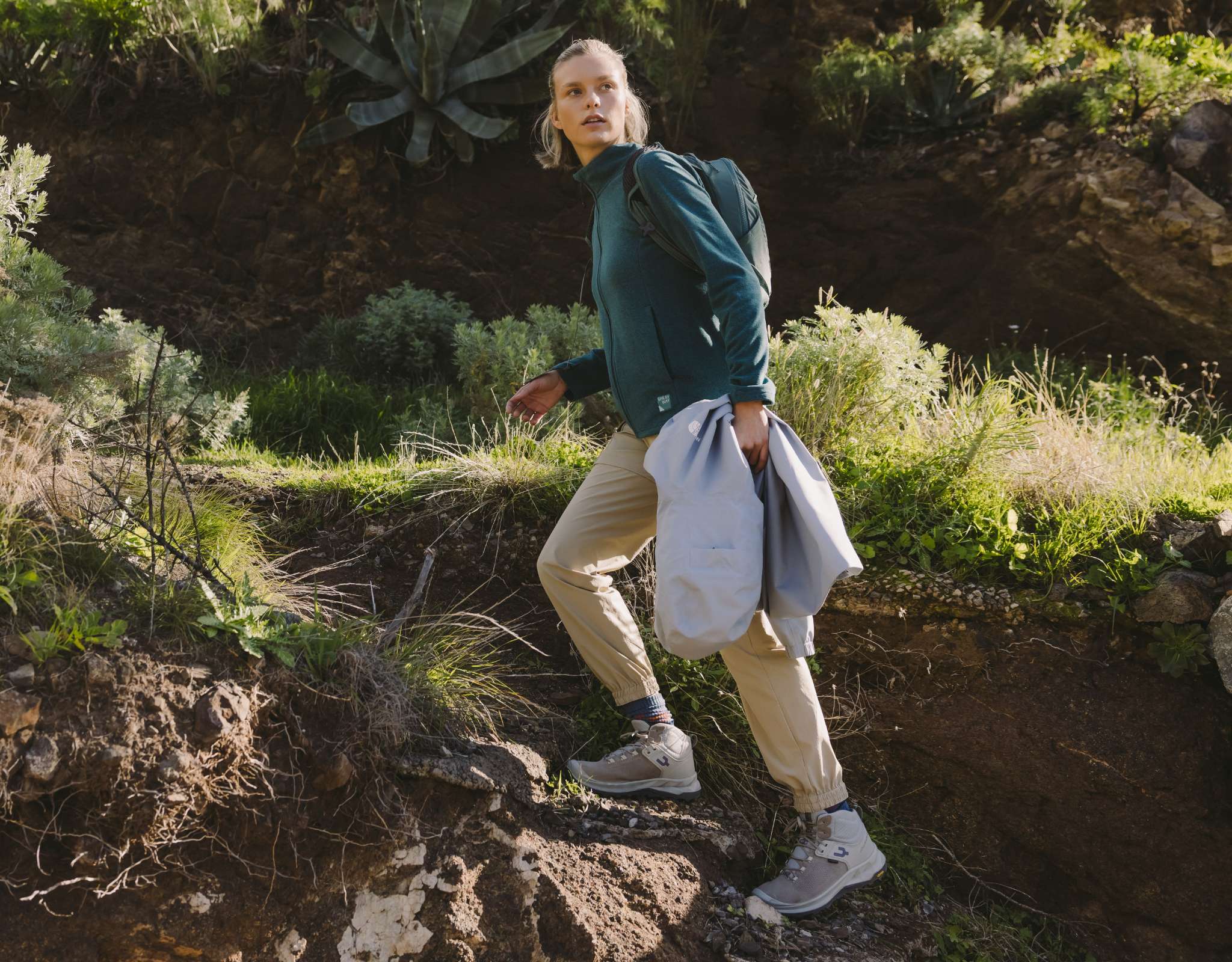 Persoon in wandelschoenen loopt op onverhard pad tussen begroeiing.