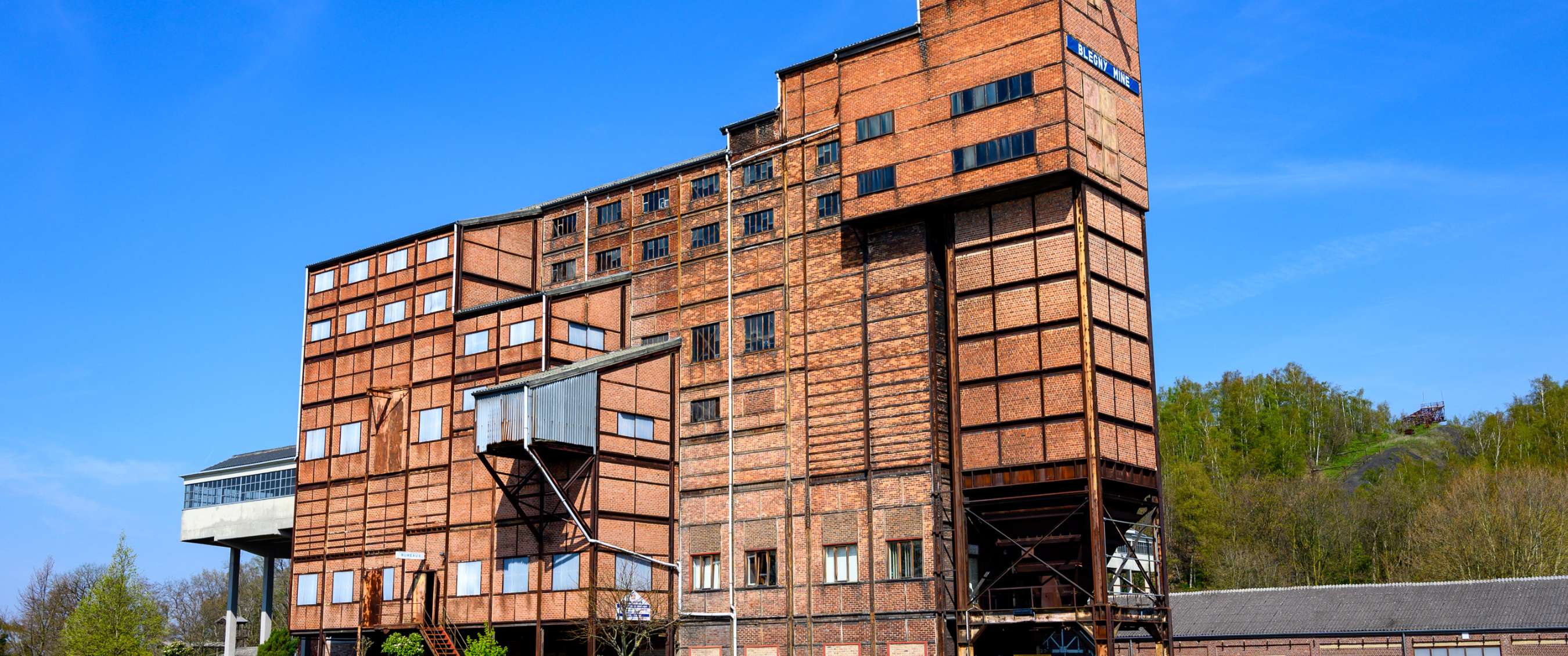 Groot historisch mijngebouw in baksteen met metalen constructies en meerdere verdiepingen.