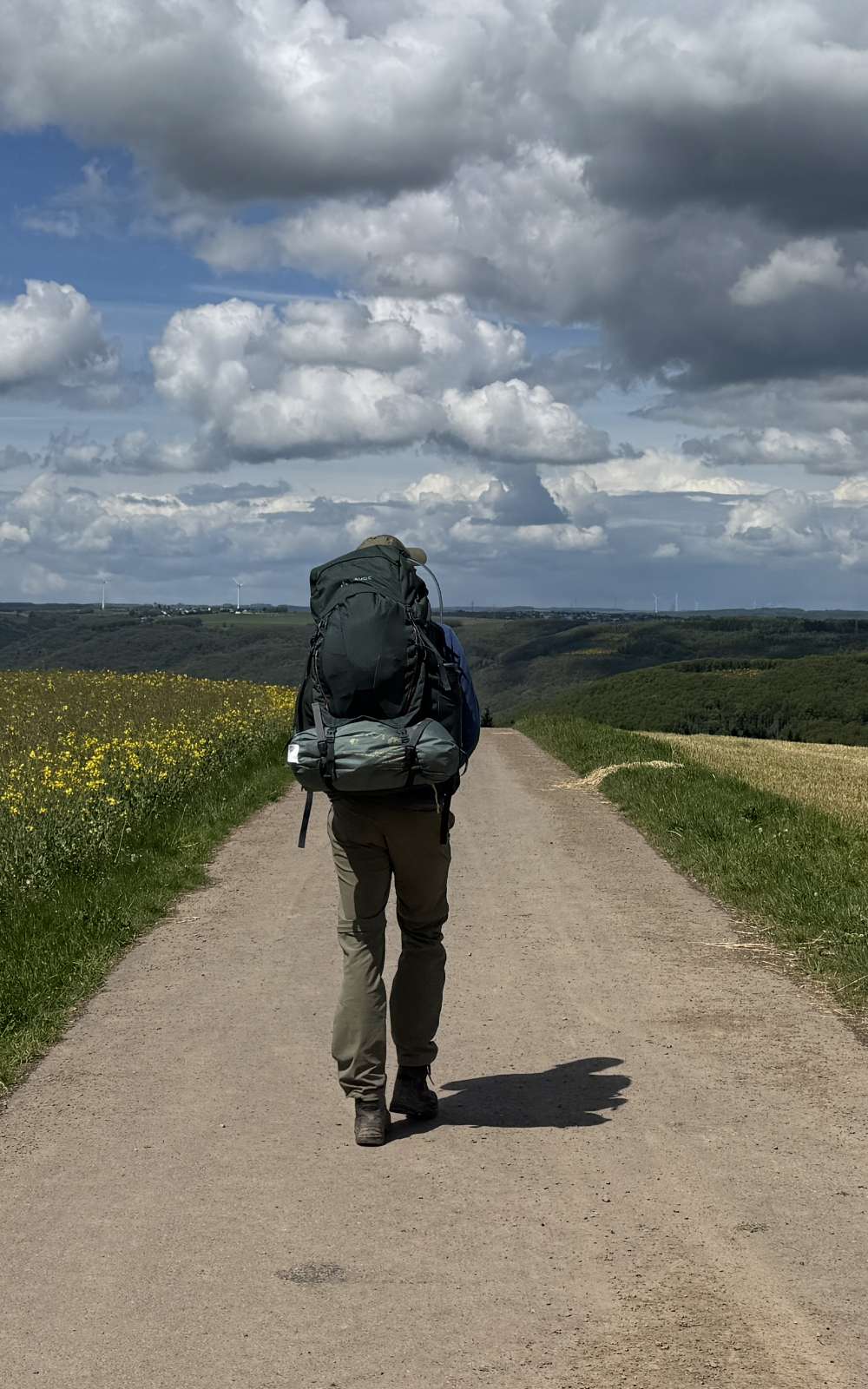 Wandelaar met grote rugzak op brede veldweg onder een wolkenlucht