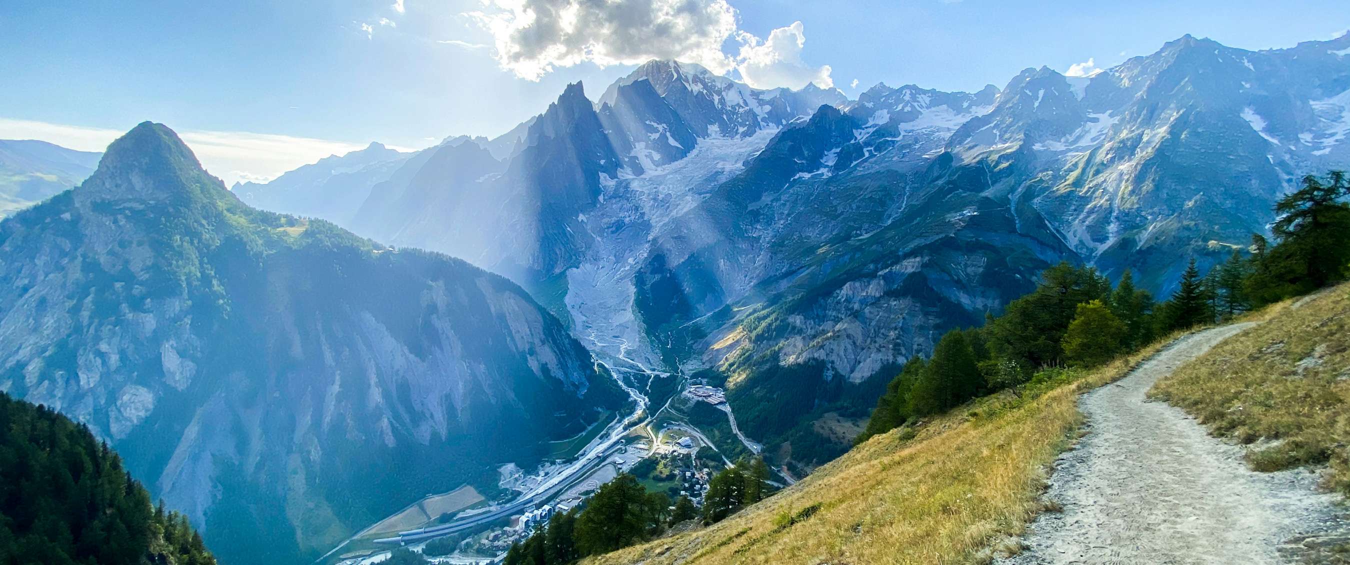 Panoramisch berglandschap met smal pad, gletsjer en zon boven de toppen.
