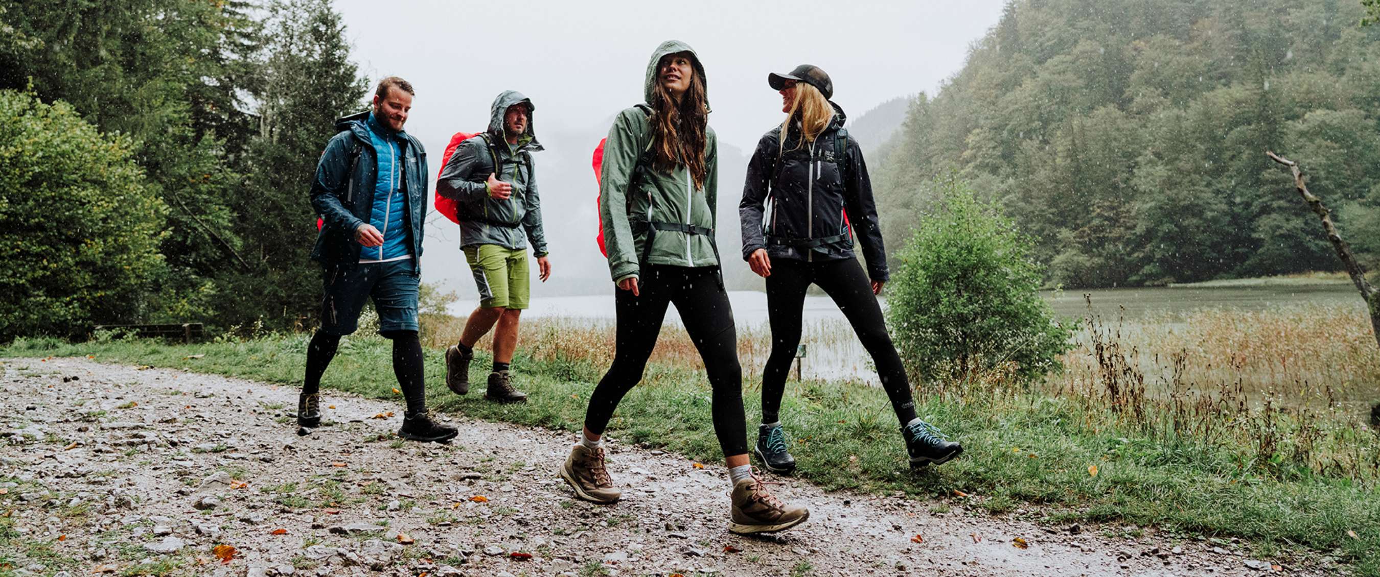 Groep wandelaars met rugzakken en regenjassen trekt door een groen landschap in de regen.