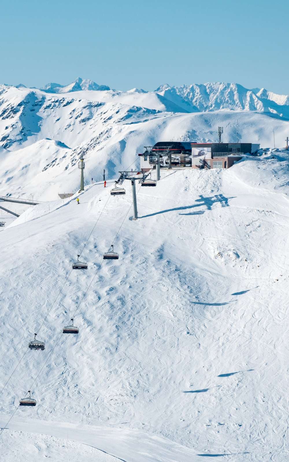 Stoeltjeslift boven een besneeuwde piste met bergtoppen op de achtergrond.