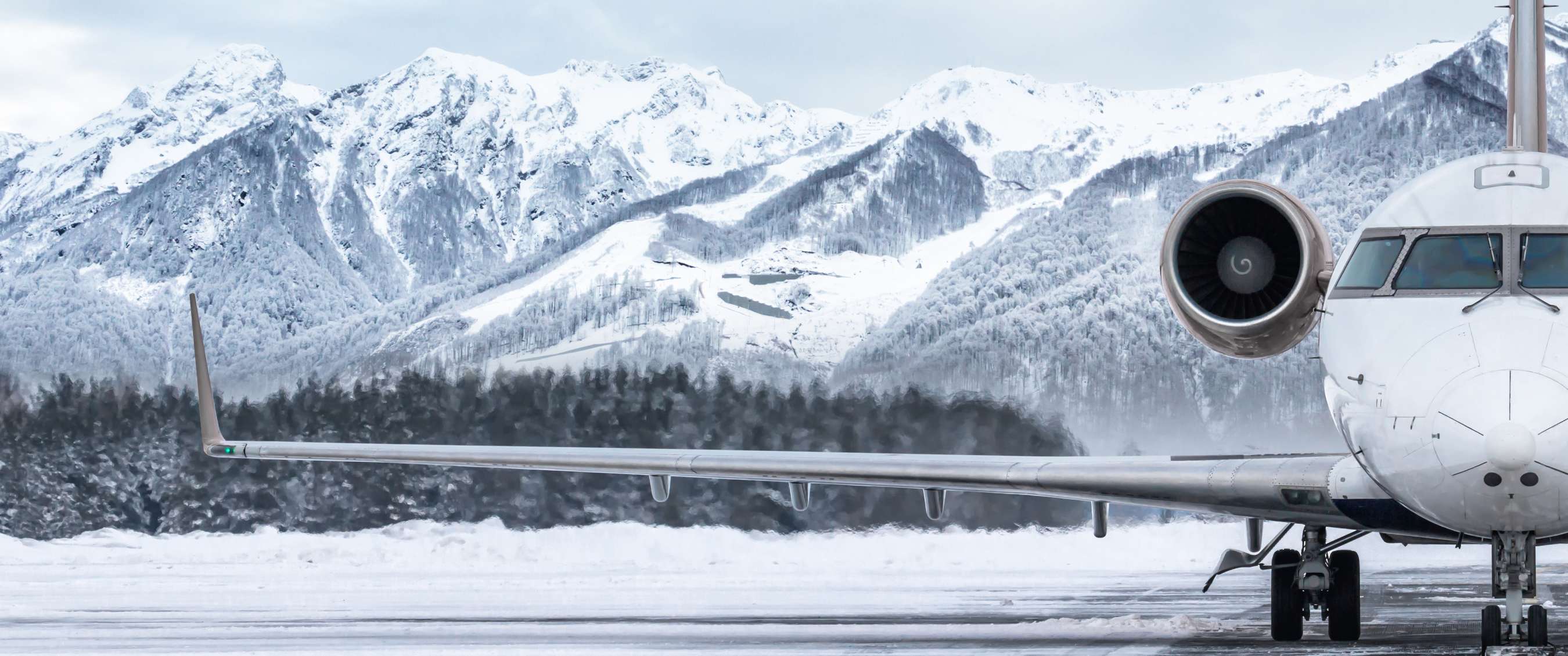 Vliegtuig staat op besneeuwde landingsbaan met bergen op de achtergrond.