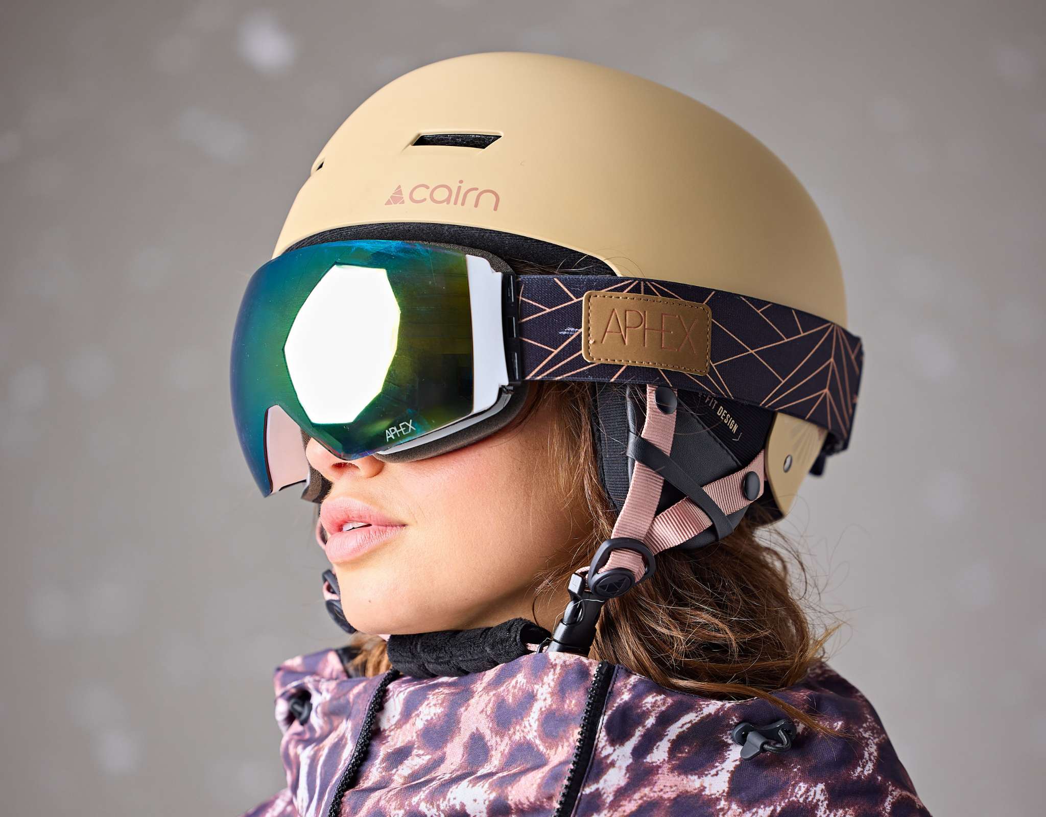 Persoon in ski-outfit buigt voorover en draagt een groene skihelm met blauwe skibril tegen een neutrale achtergrond.