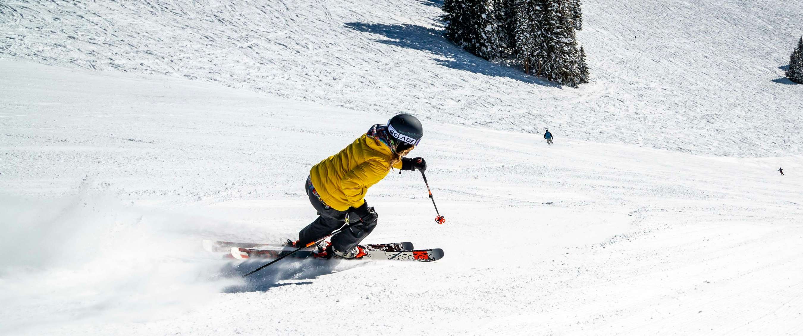 Een skiër in een gele jas en zwarte handschoenen maakt een bocht op een besneeuwde piste.