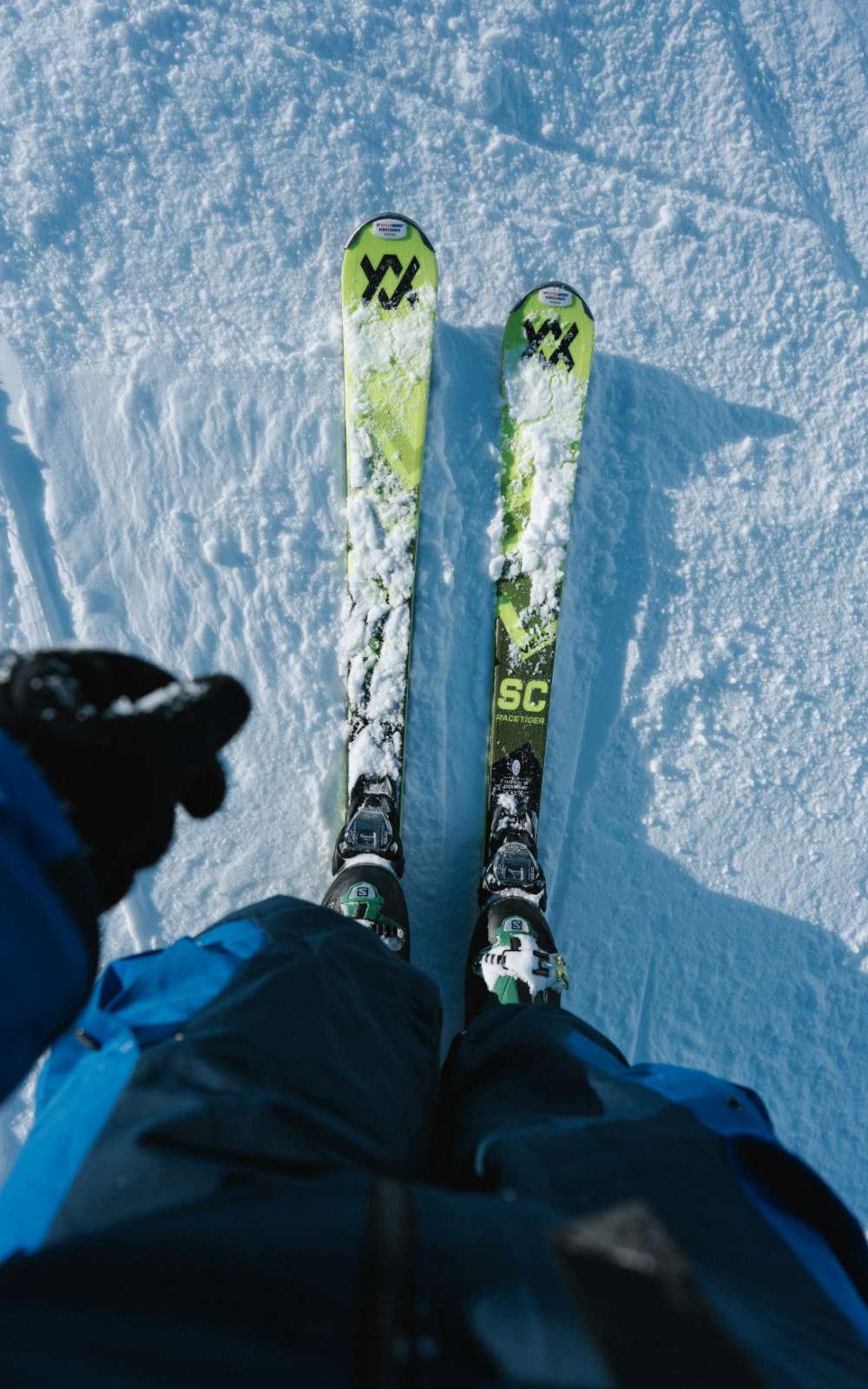 Van bovenaf gezien: twee groene ski's met sneeuw erop en skischoenen in de bindingen.