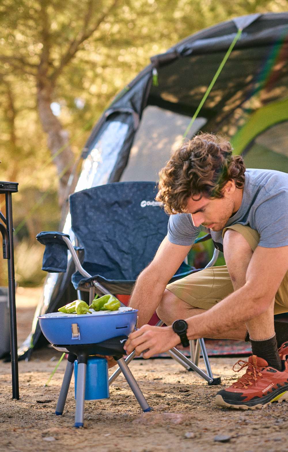 Man stelt een kleine barbecue in op een camping naast een tent